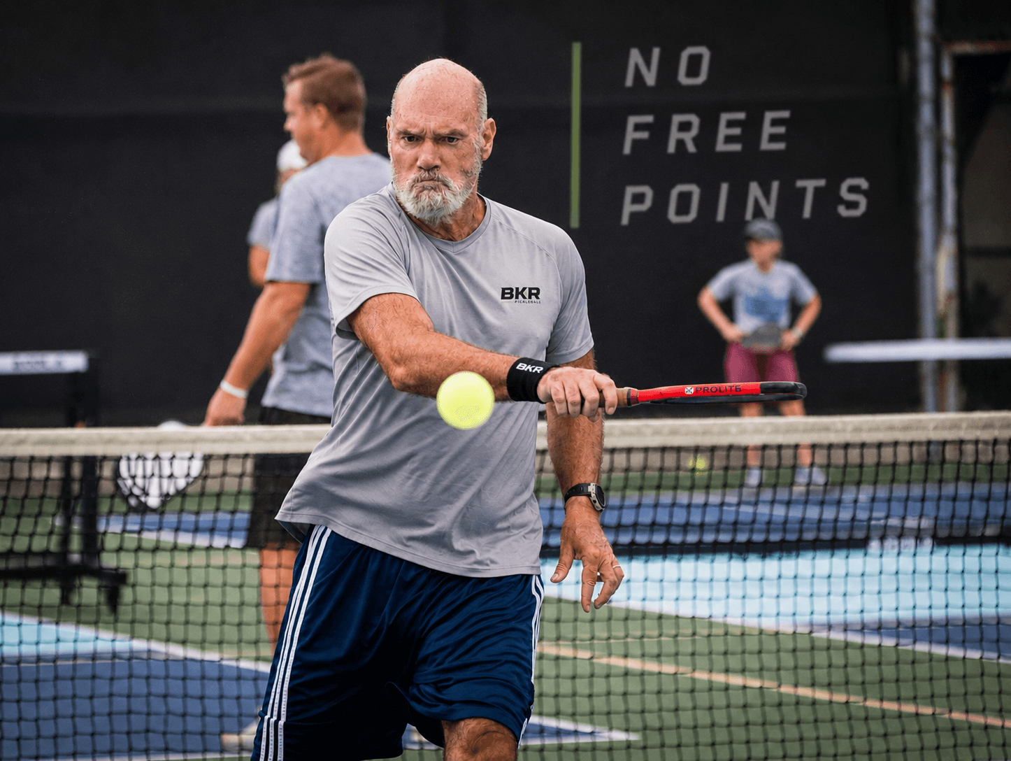 Paul hitting a backhand at the kitchen line with the BKR / No Free Points banner behind him