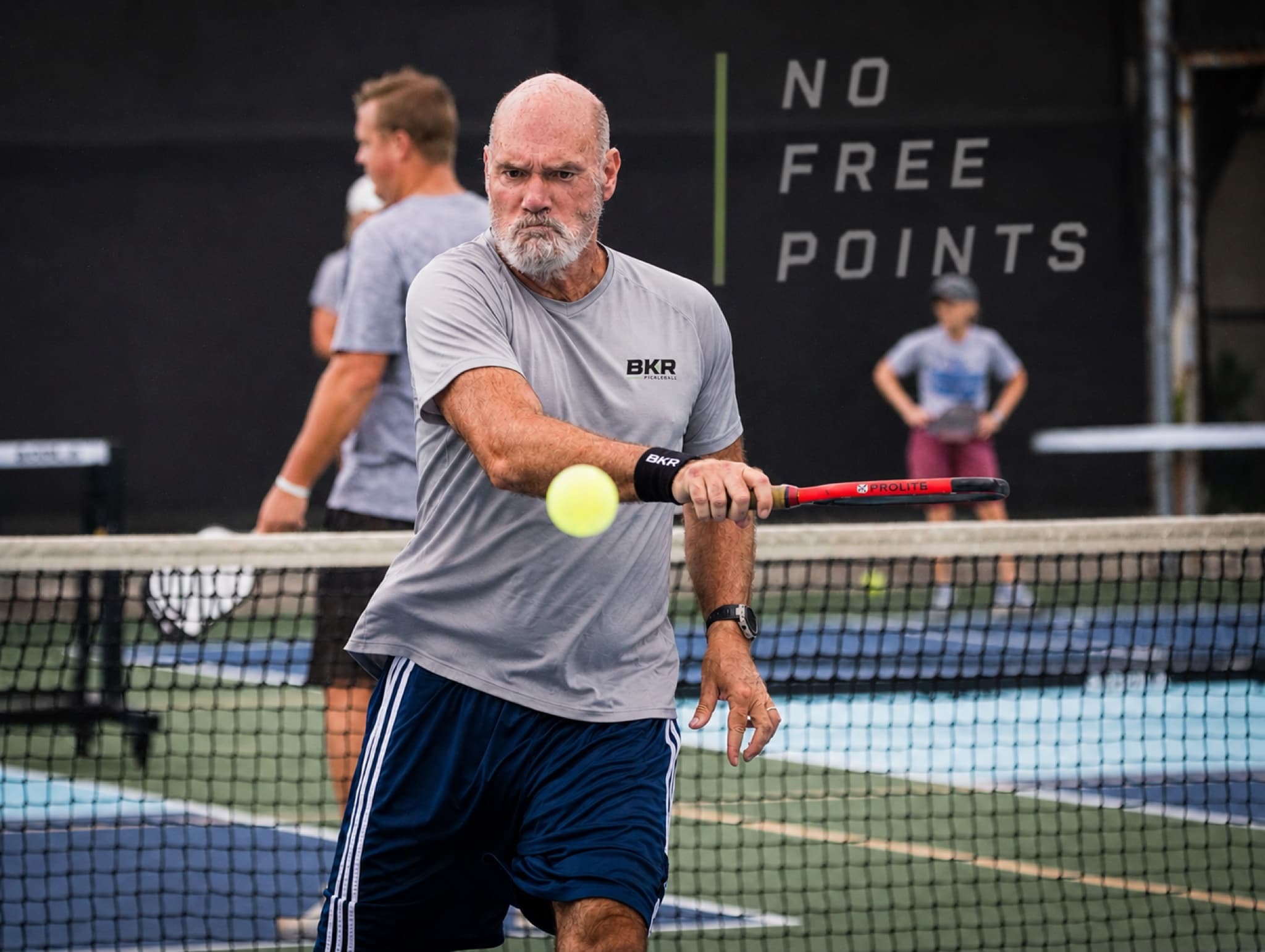 Paul Baker driving a backhand at the kitchen line, with the NO FREE POINTS wall behind